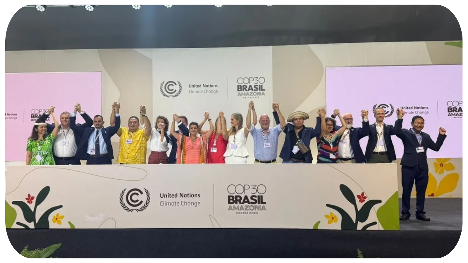 Group of people on stage at COP30 Brazil Amazonia climate conference, holding hands and raising them in celebration or unity, with banners displaying United Nations Climate Change and COP30 Brasil Amazonas logos in the background.