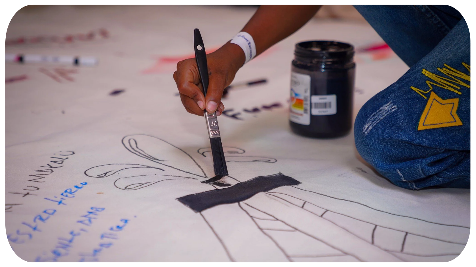 Person drawing with black paint on a large sheet of paper, creating a picture of a bunny with long ears and a rectangular body, with the words 'TUNDELIJO' and '¡NO! que yo' written on the paper.
