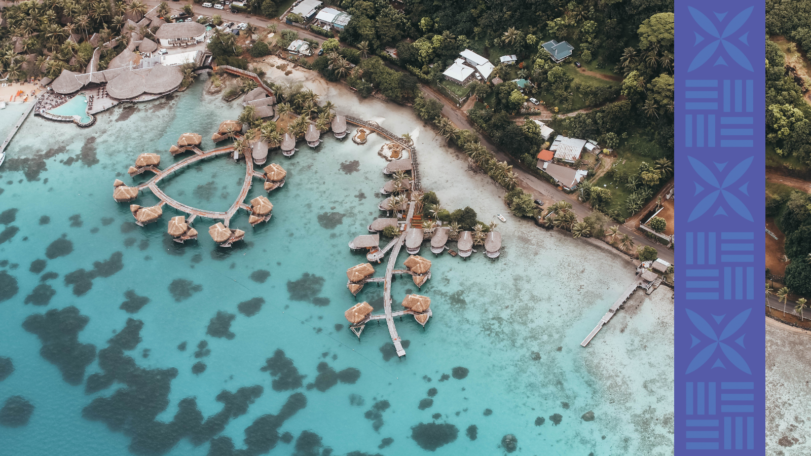Aerial view of a tropical resort with overwater bungalows, swim lagoon, and a lush green surrounding landscape.