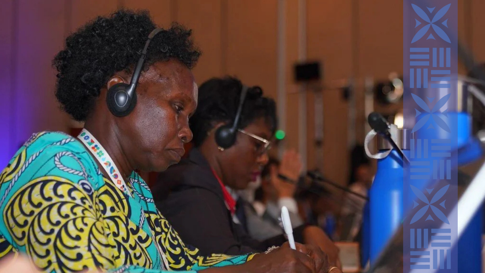 Three women attending a conference, sitting at a table with microphones, wearing headsets, and taking notes.