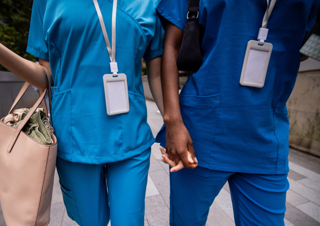 Two healthcare workers in blue scrubs holding hands