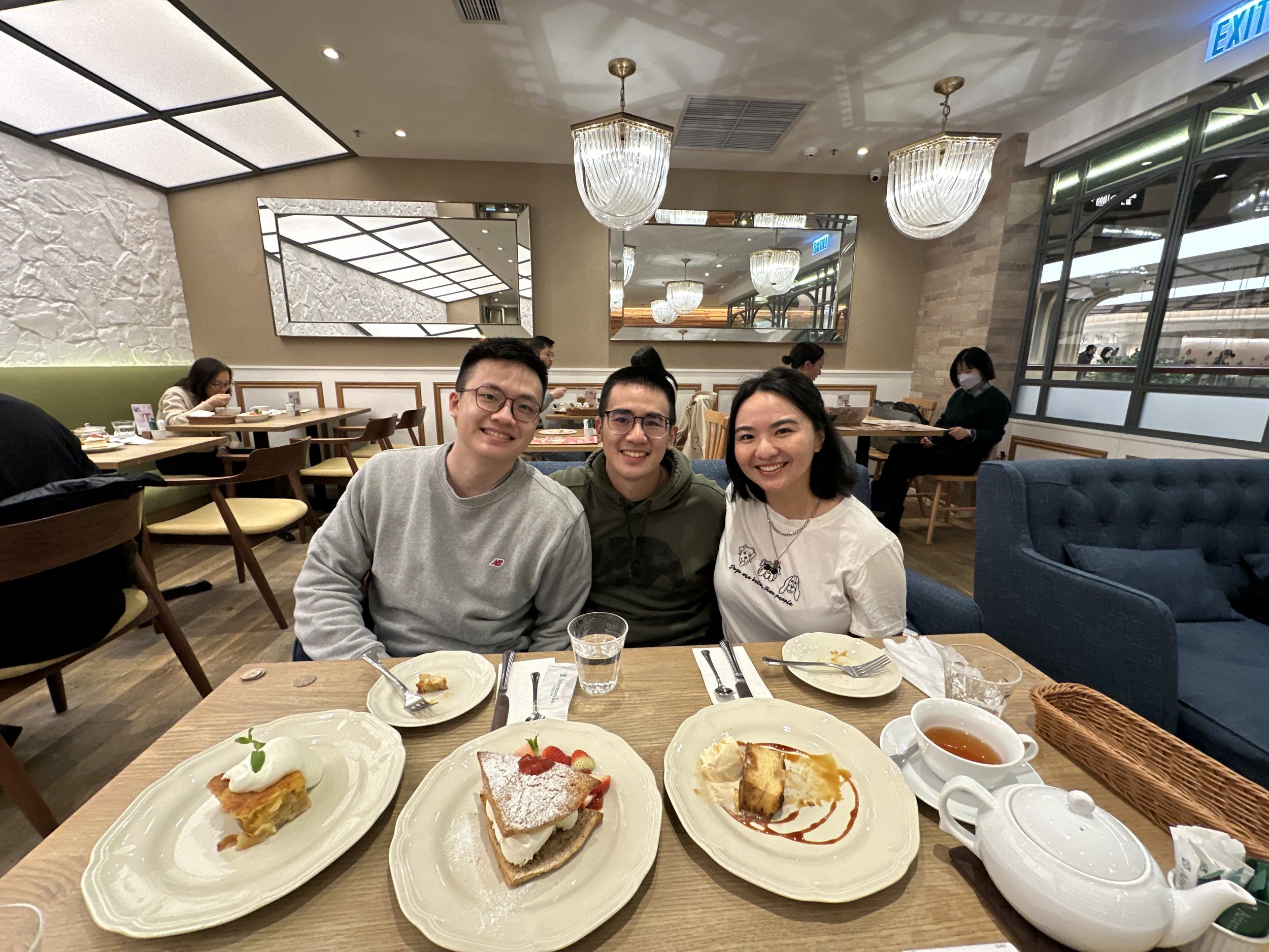 Three friends sitting at a restaurant table with desserts and drinks, smiling for the photo.
