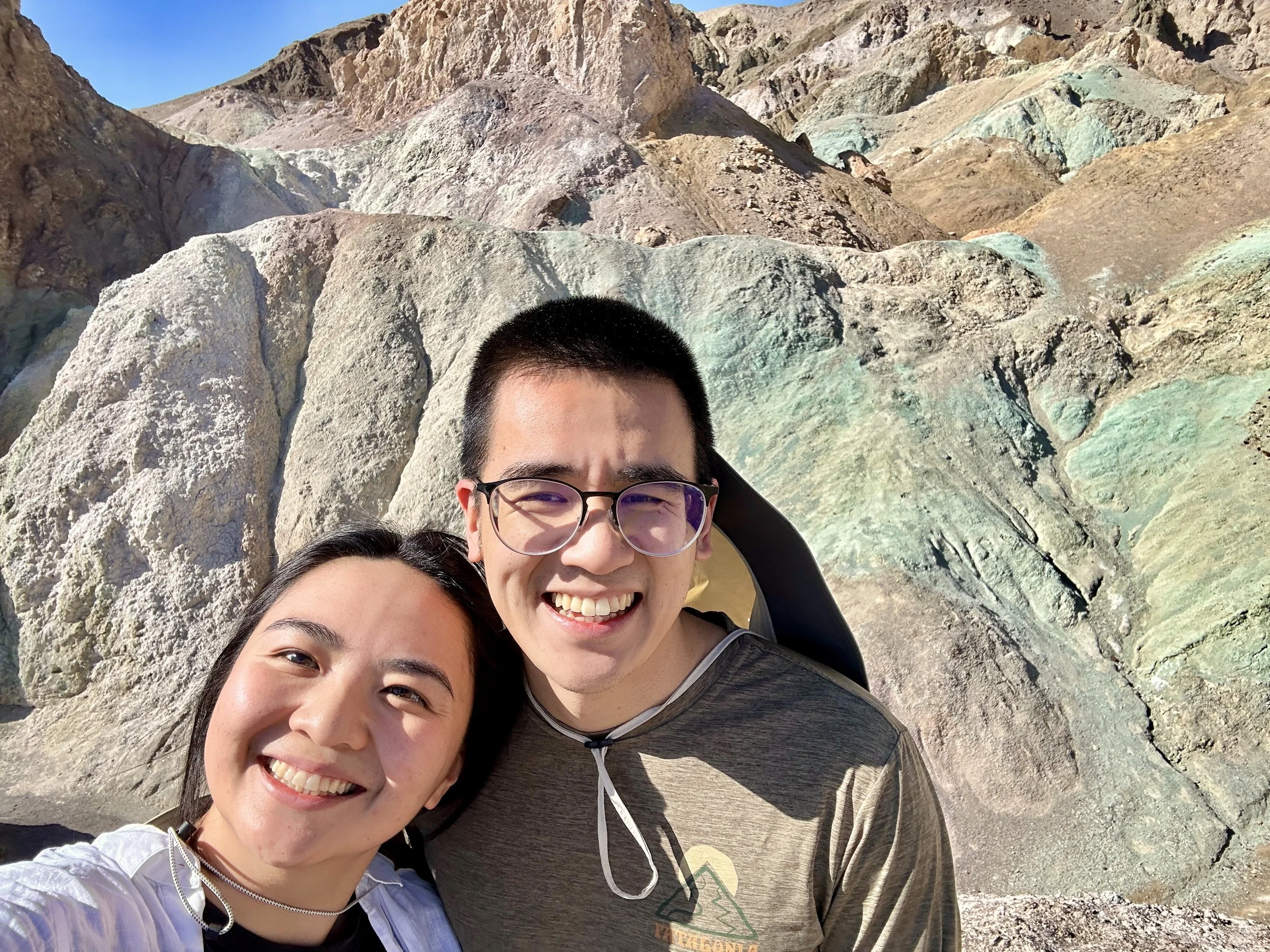 Three people smiling and taking a selfie with rocky desert landscape in the background.