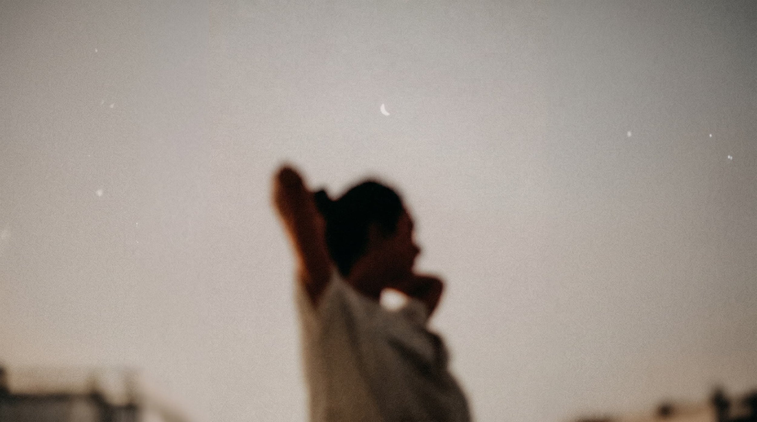 A person with long hair, dressed in a white top, running along a street at dusk or dawn, with a crescent moon and stars visible in the sky.
