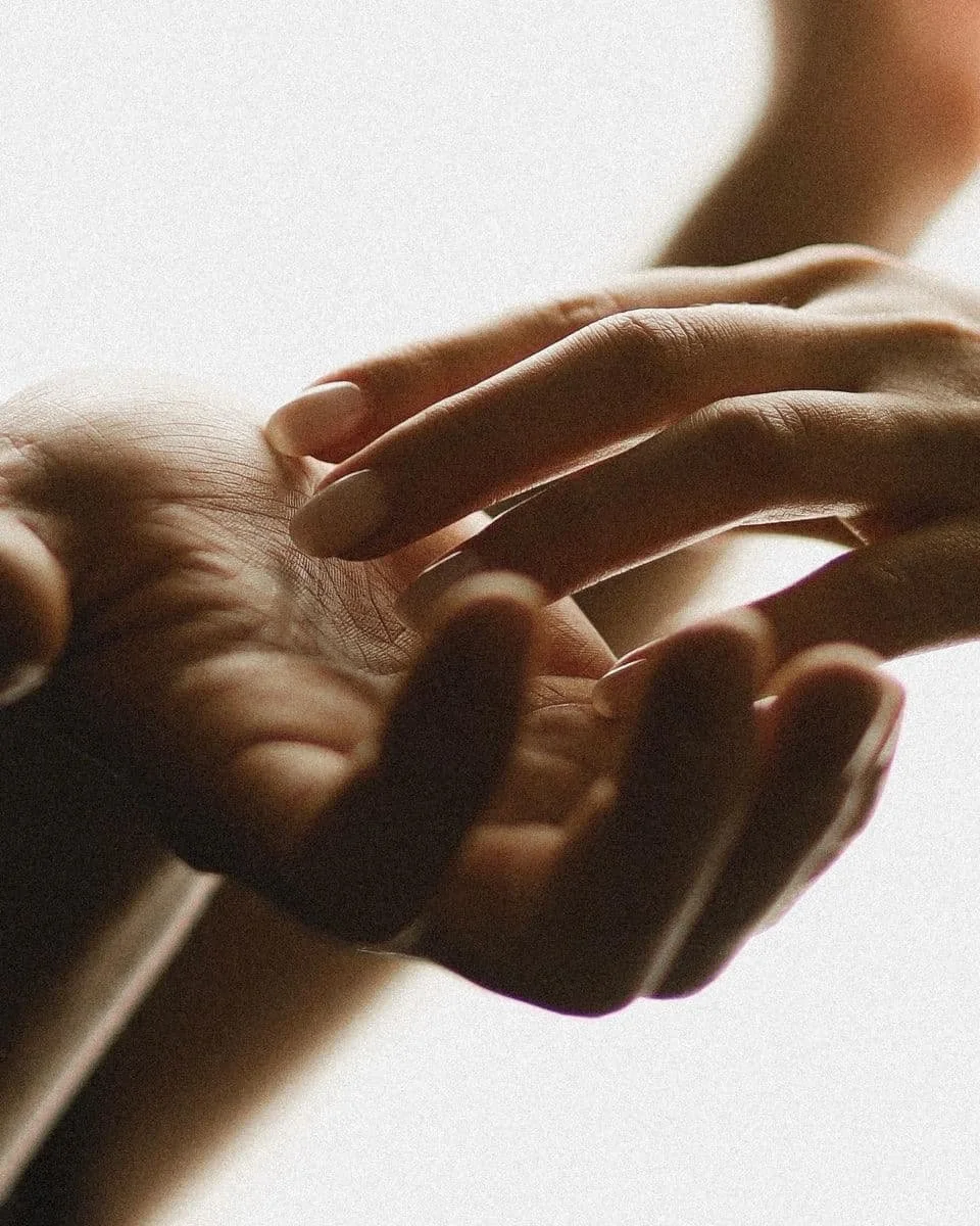 Close-up of two hands gently touching against a plain background.