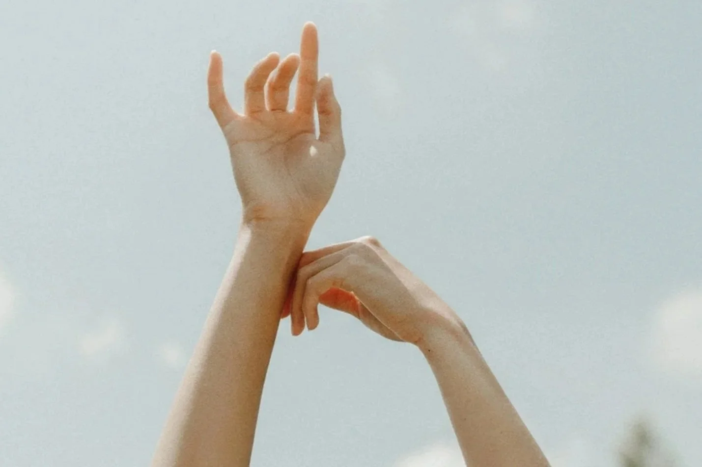 Two hands reaching upward against a blue sky background with a few clouds.