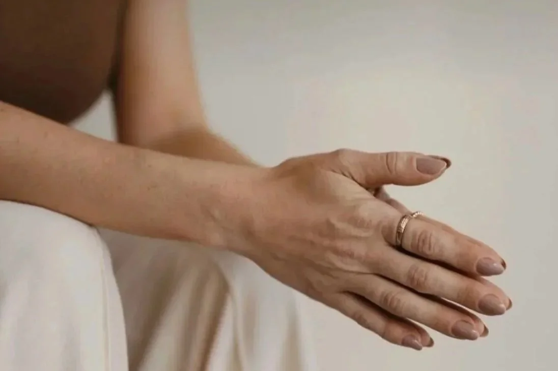 Close-up of a person's hand resting on their knee, with a ring on their finger.
