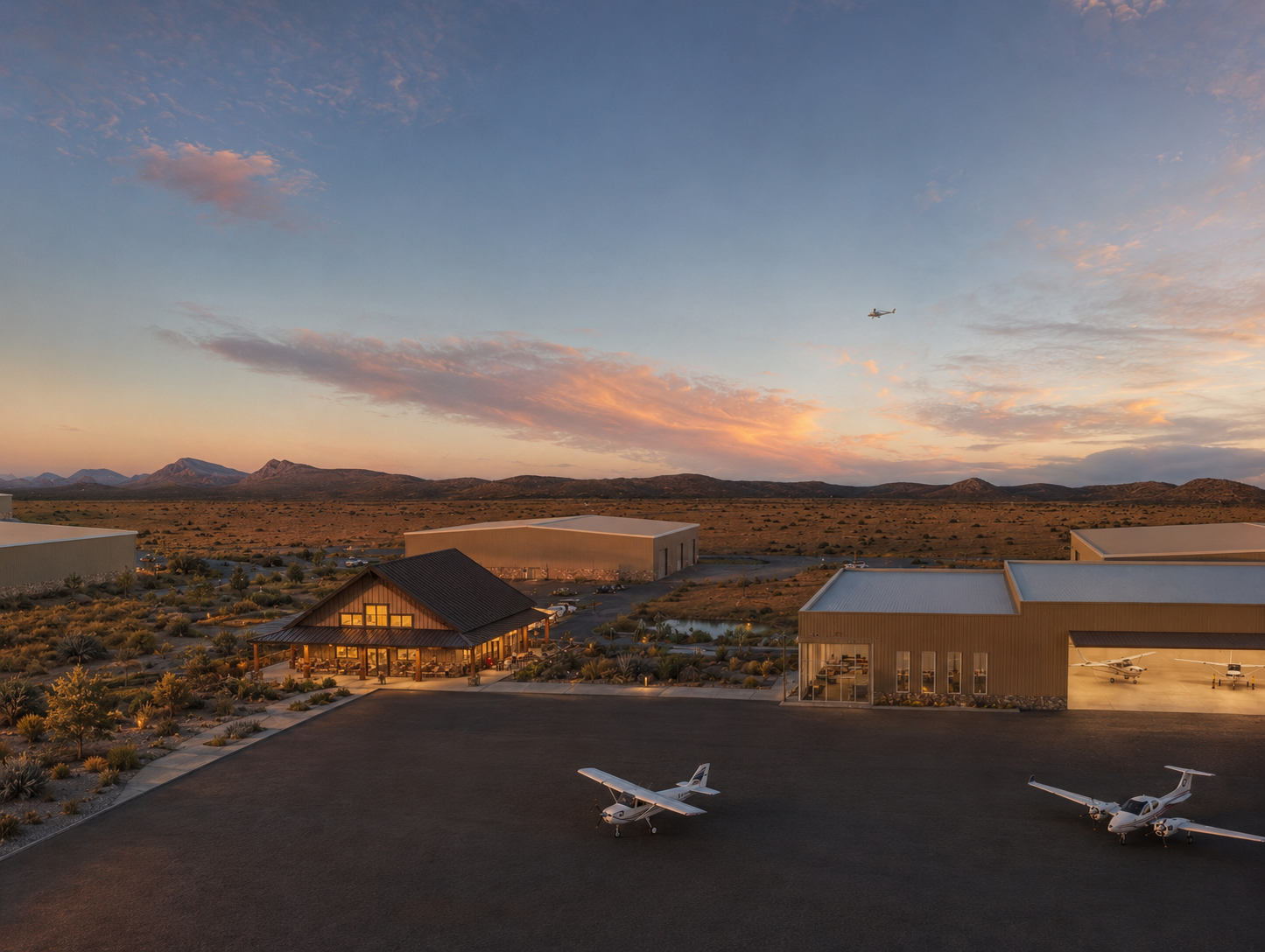 A small airport or airstrip in a desert landscape at sunset, with a building, airplanes on the tarmac, and mountains in the background, and a helicopter and airplane flying in the sky.