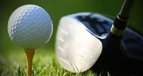 Golf ball on tee next to golf club on grass
