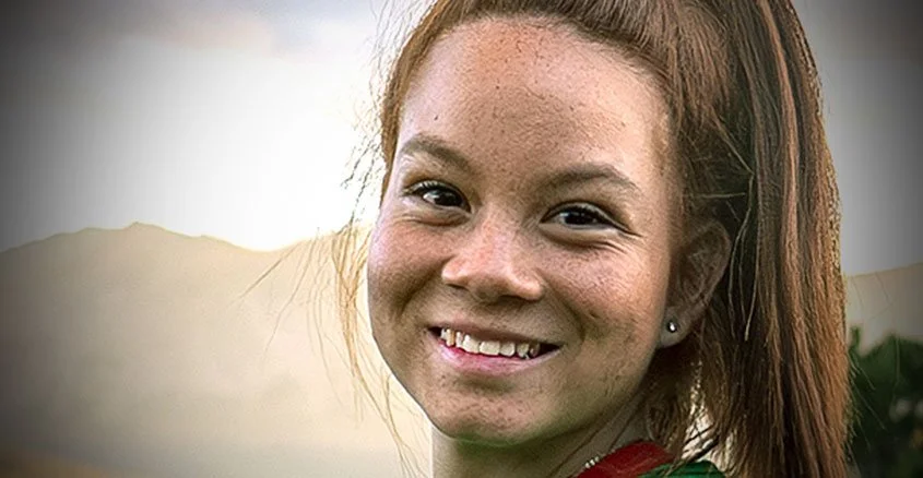 Smiling young girl with red hair and freckles outdoors in natural light.