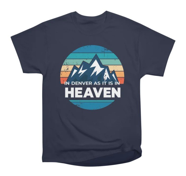 A navy blue t-shirt with a graphic of mountain peaks inside a circle with colorful horizontal stripes in the background. It has the text 'In Denver as it is in HEAVEN' printed on it.