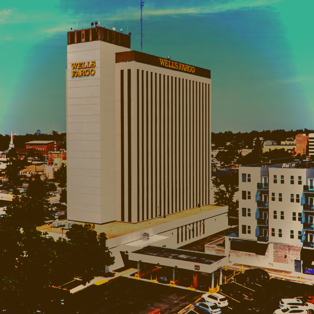 Tall building with "WELLS FARGO" signs on top, surrounded by smaller buildings and parked cars.