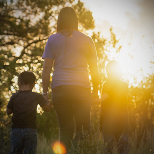 Family walking outside during sunset with two children holding hands with an adult, silhouetted by the sunlight.
