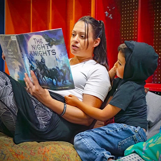 Woman and young boy reading a book titled 'The Night Knights' together in a cozy room