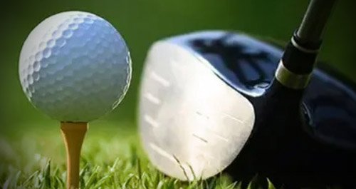 Golf ball on tee and golf club on grass.