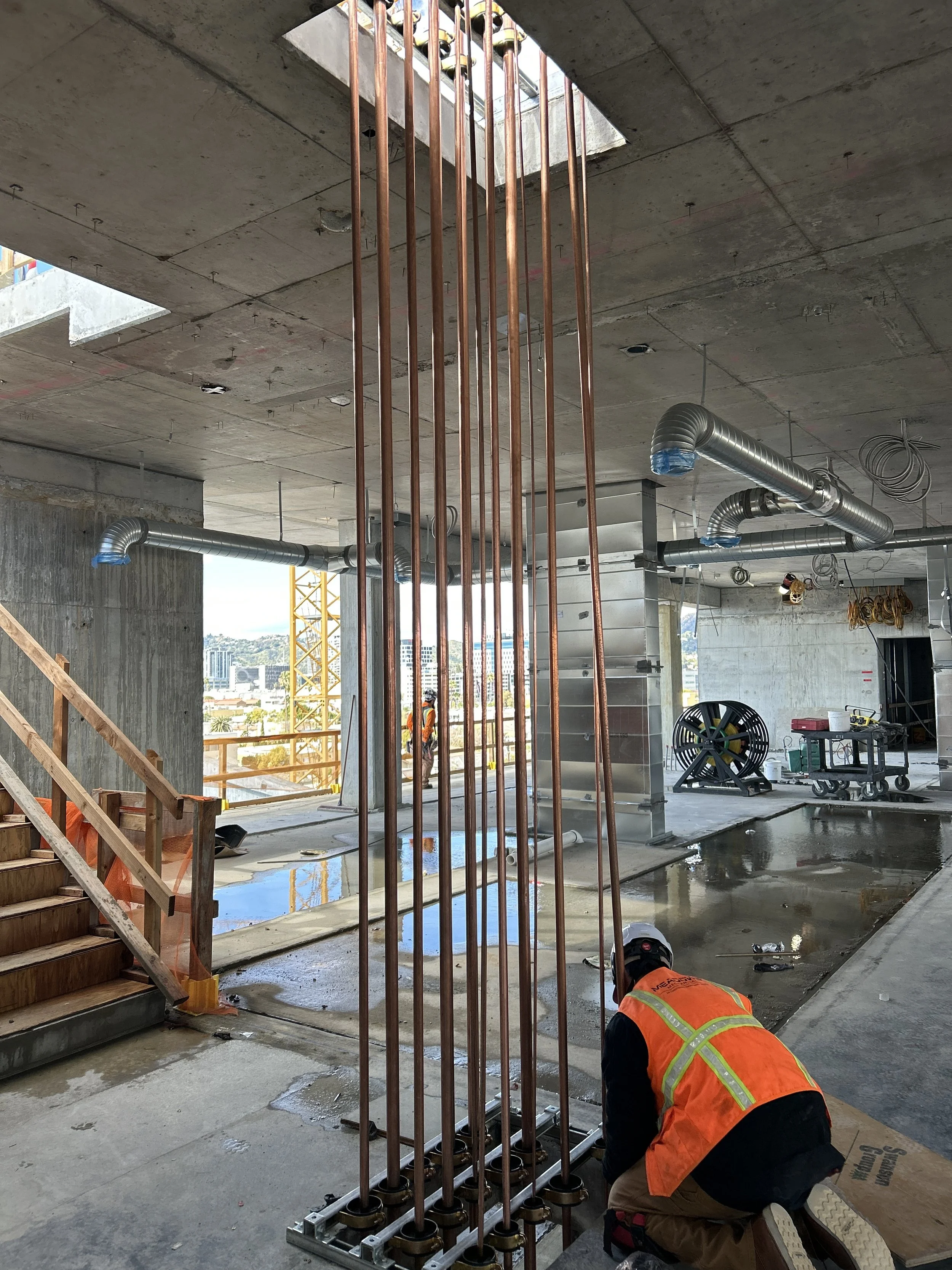 Construction workers building and installing copper piping within a concrete structure of a building under construction.