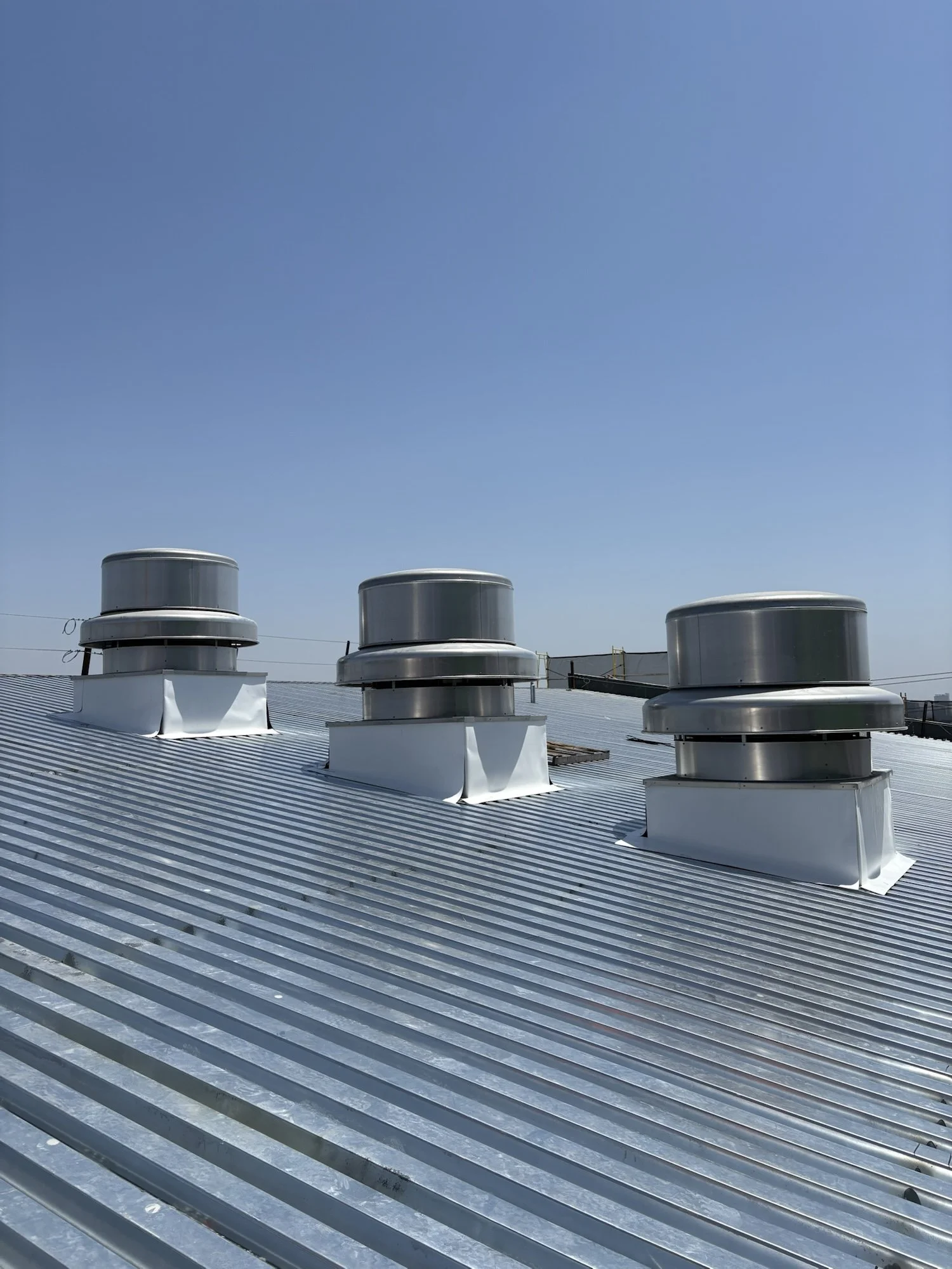 A rooftop with multiple industrial HVAC units and vents installed on a metal roof under a clear blue sky.