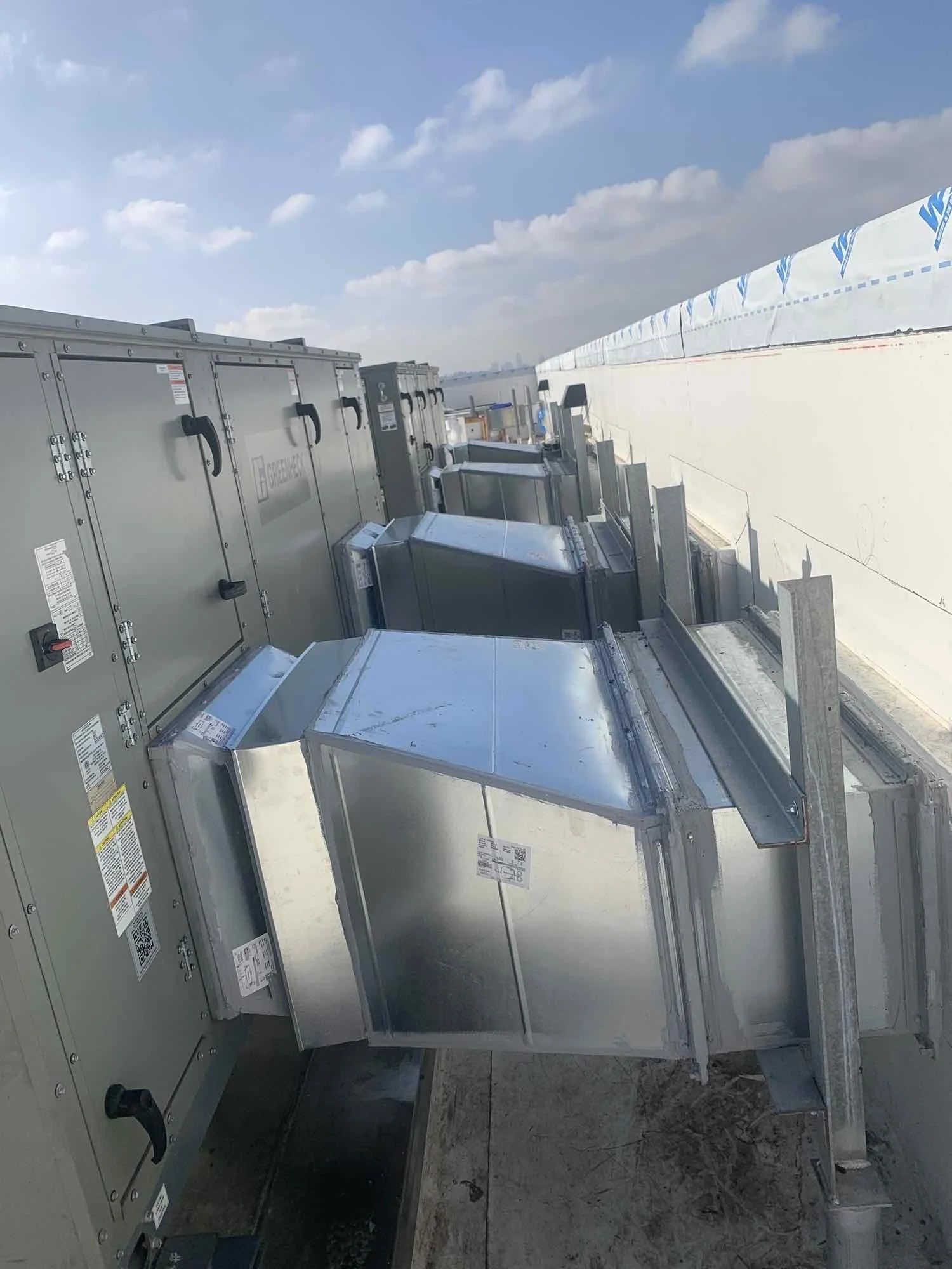 Variety of industrial HVAC and ventilation units installed on a rooftop under a partly cloudy sky.