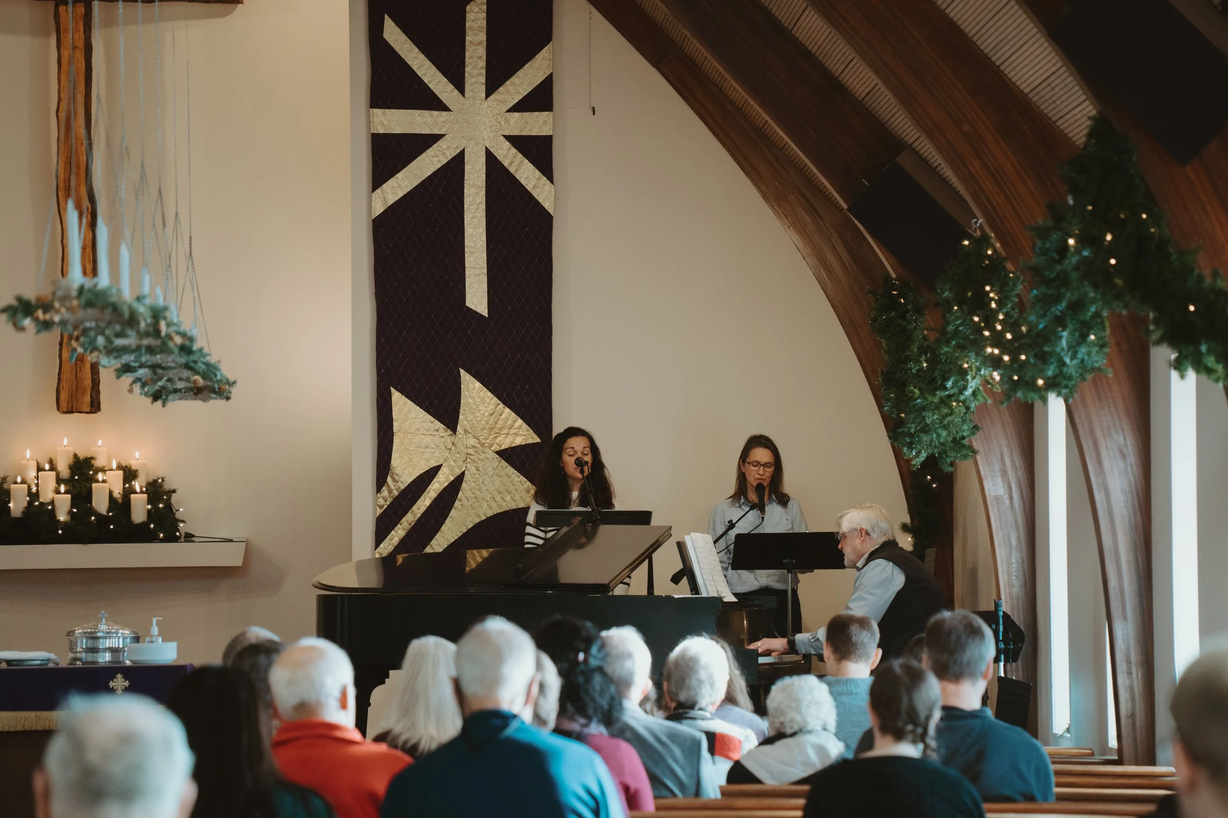 People singing at a church service, with Christmas decorations and a large banner featuring a Christian symbol in the background.