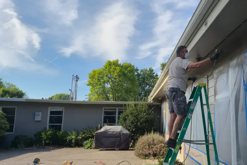 A man standing on a ladder sprays paint on the church building at Calvin Presbyterian in Corvallis, Oregon.
