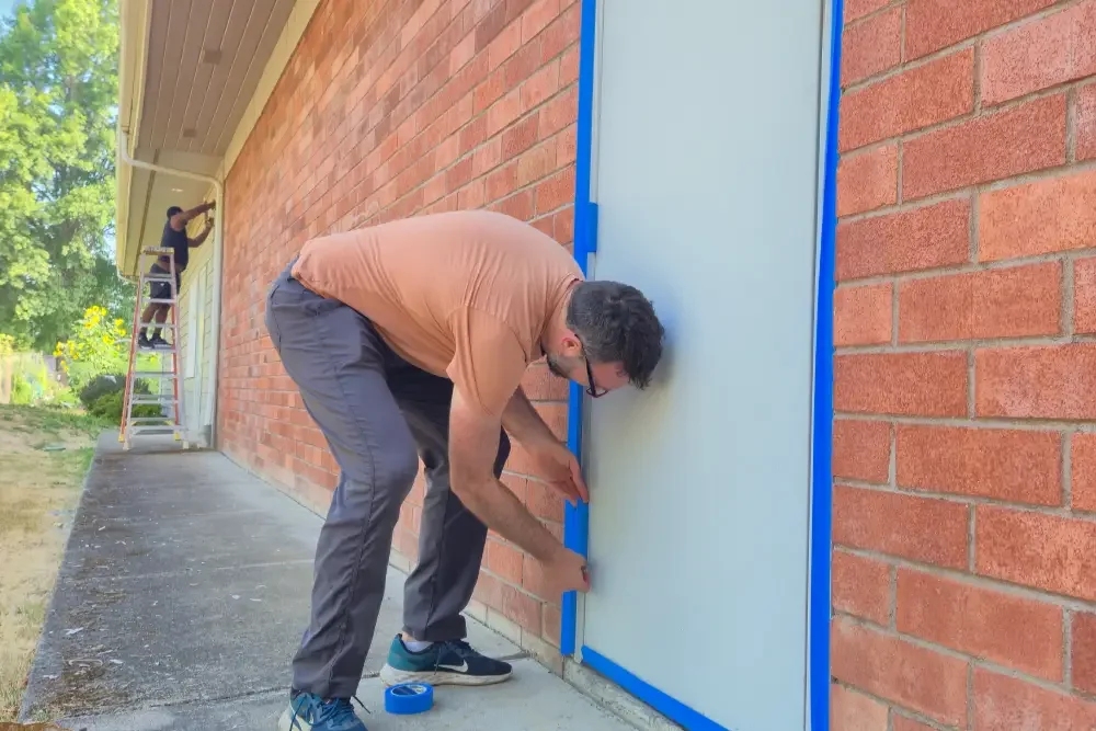 Men paint doors on a brick wall to prepare it for painting at Calvin Presbyterian Church.