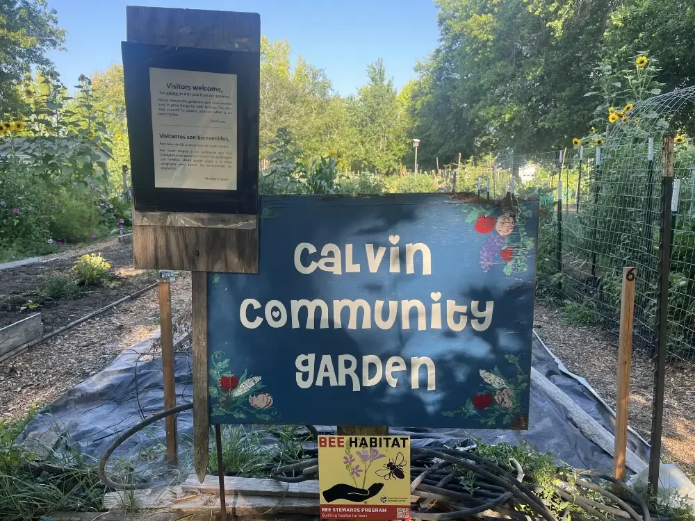 Sign for Calvin Community Garden with a visitor welcome notice, and a smaller sign about bee habitat.