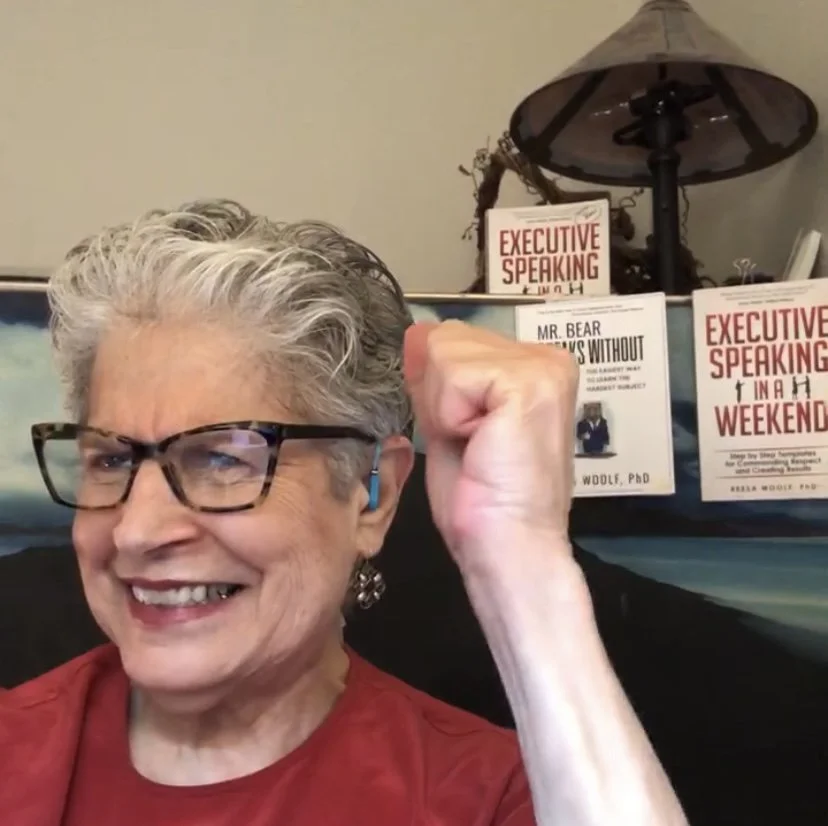 A smiling expert to stop Public Speaking Fear. Behind her are her two books titled 'Executive Speaking' and 'Mr. Bear Talks Without Fear."