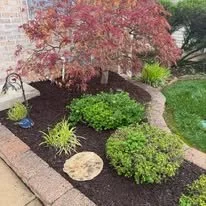 A garden with a pink-leafed tree, green bushes, and a stone pathway, bordered by a brick edging.