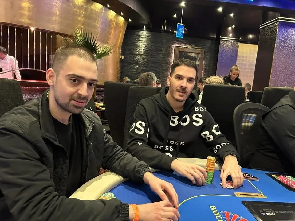 Two men sitting at a poker table with stacks of chips during a casino game.