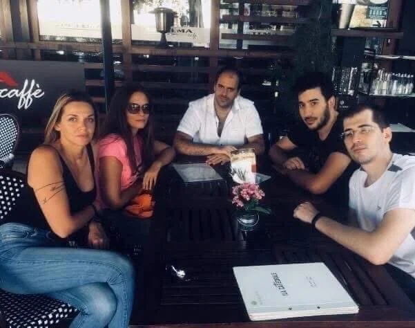 Five people sitting at a table in a restaurant, with a small bouquet of pink flowers and a menu on the table.