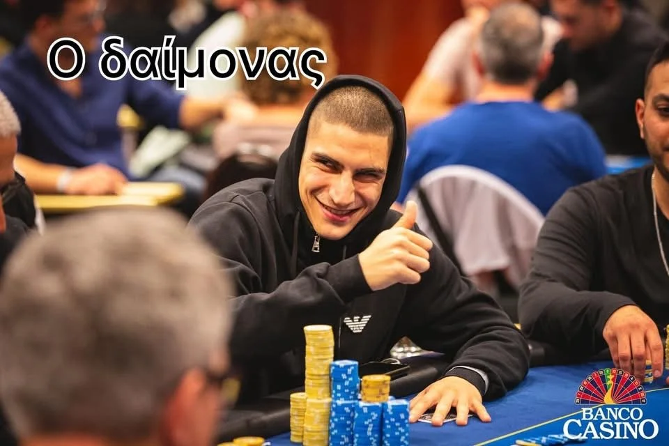 Young man smiling and giving a thumbs-up at a poker table with poker chips, in a bustling casino or poker room.