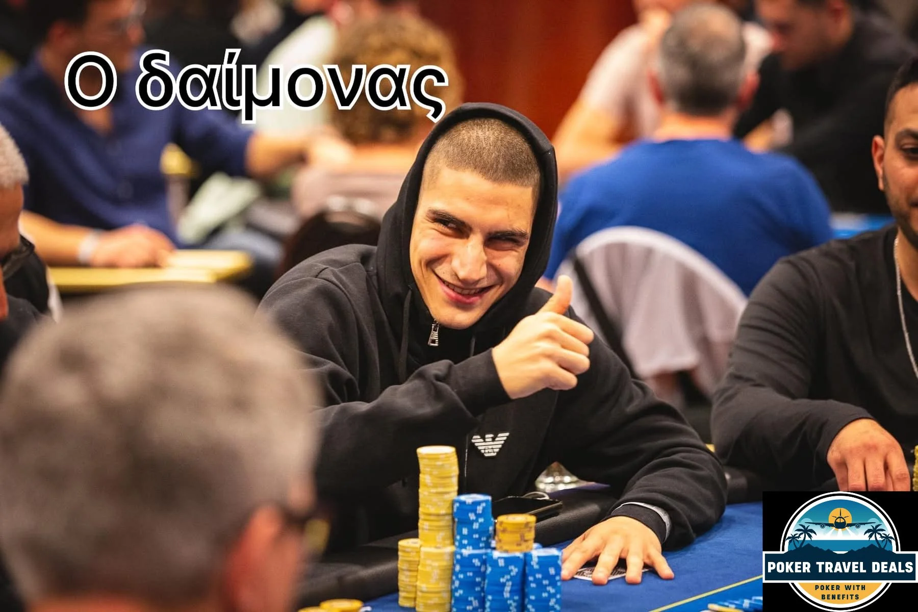 A young man with a short buzz cut hairstyle and a black hoodie smiling and giving a thumbs-up gesture at a poker tournament, with colorful poker chips in front of him.