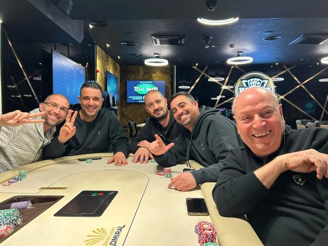 Five men smiling and posing at a poker table with poker chips in a casino.