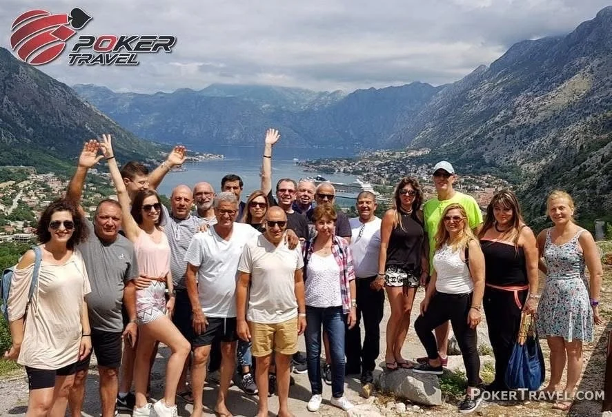 Group of people posing outdoors on a scenic mountain overlook with a lake and mountains in the background.