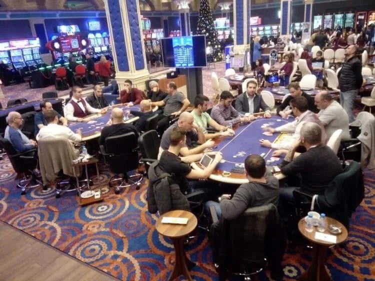 People playing poker at a casino table decorated with a Christmas tree, with slot machines in the background.