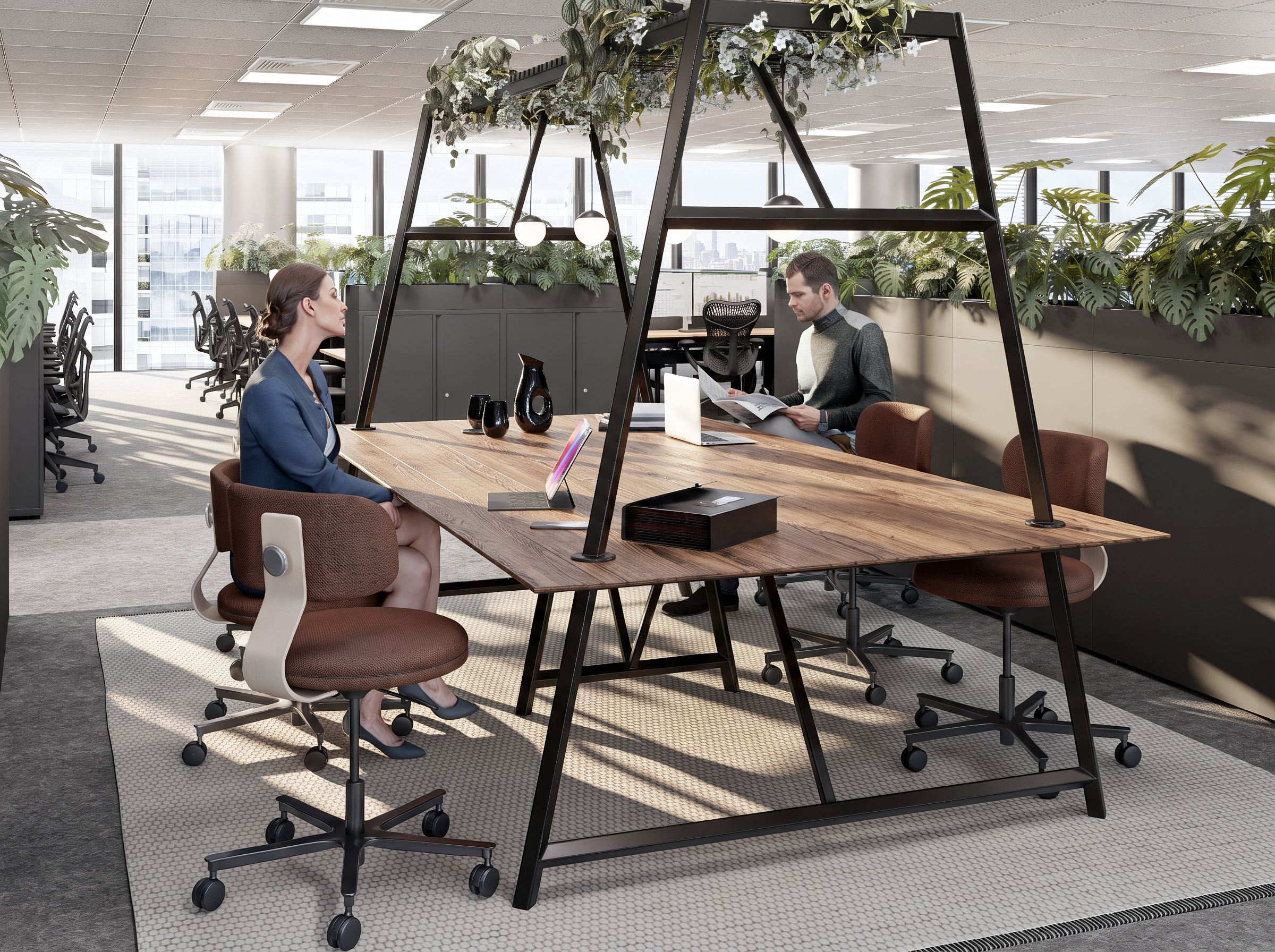 Office space with two people sitting at a wooden table, surrounded by large green plants and natural light from windows.