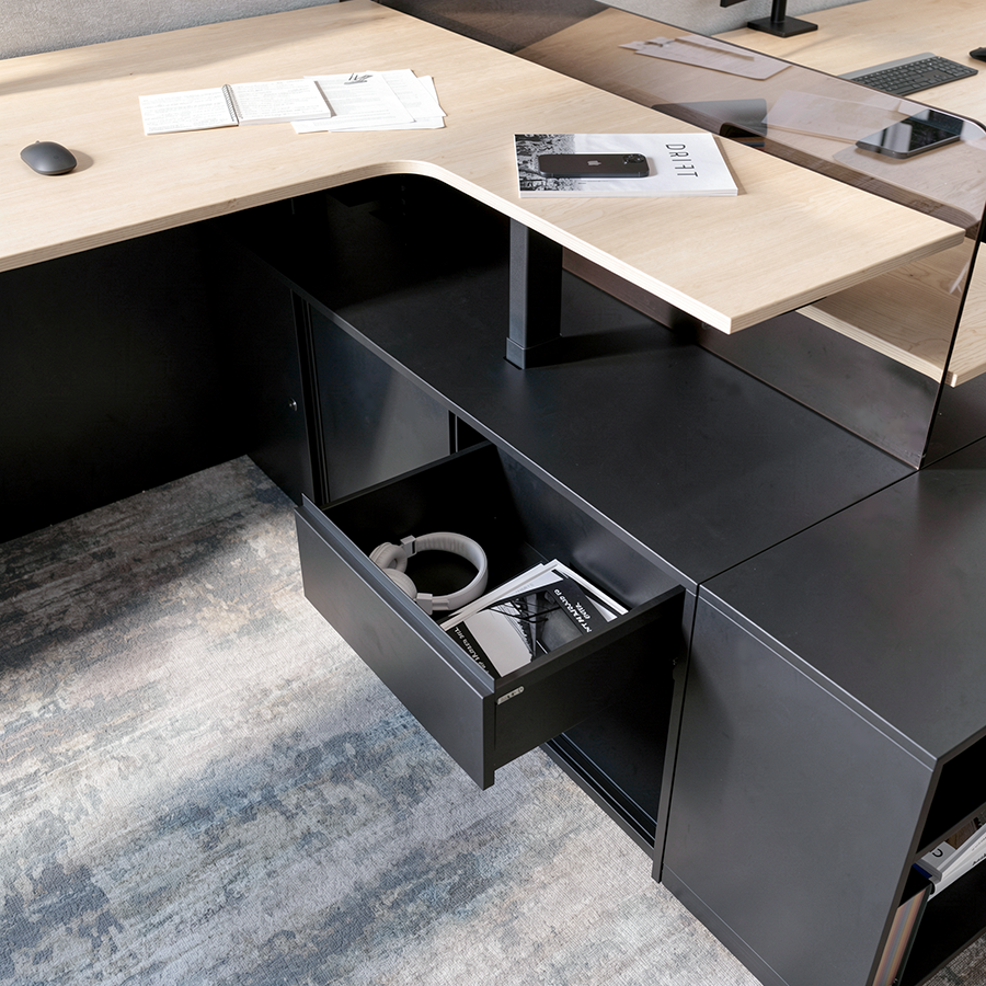 Office desk with a computer mouse, paperwork, a smartphone, a planner, and a laptop on top, and a black drawer with headphones and a magazine underneath.