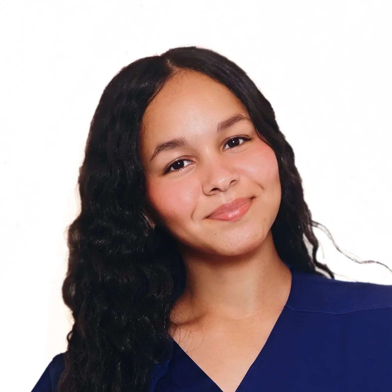 A woman with medium skin, black wavy hair, wearing a dark blue top, smiling against a plain white background.