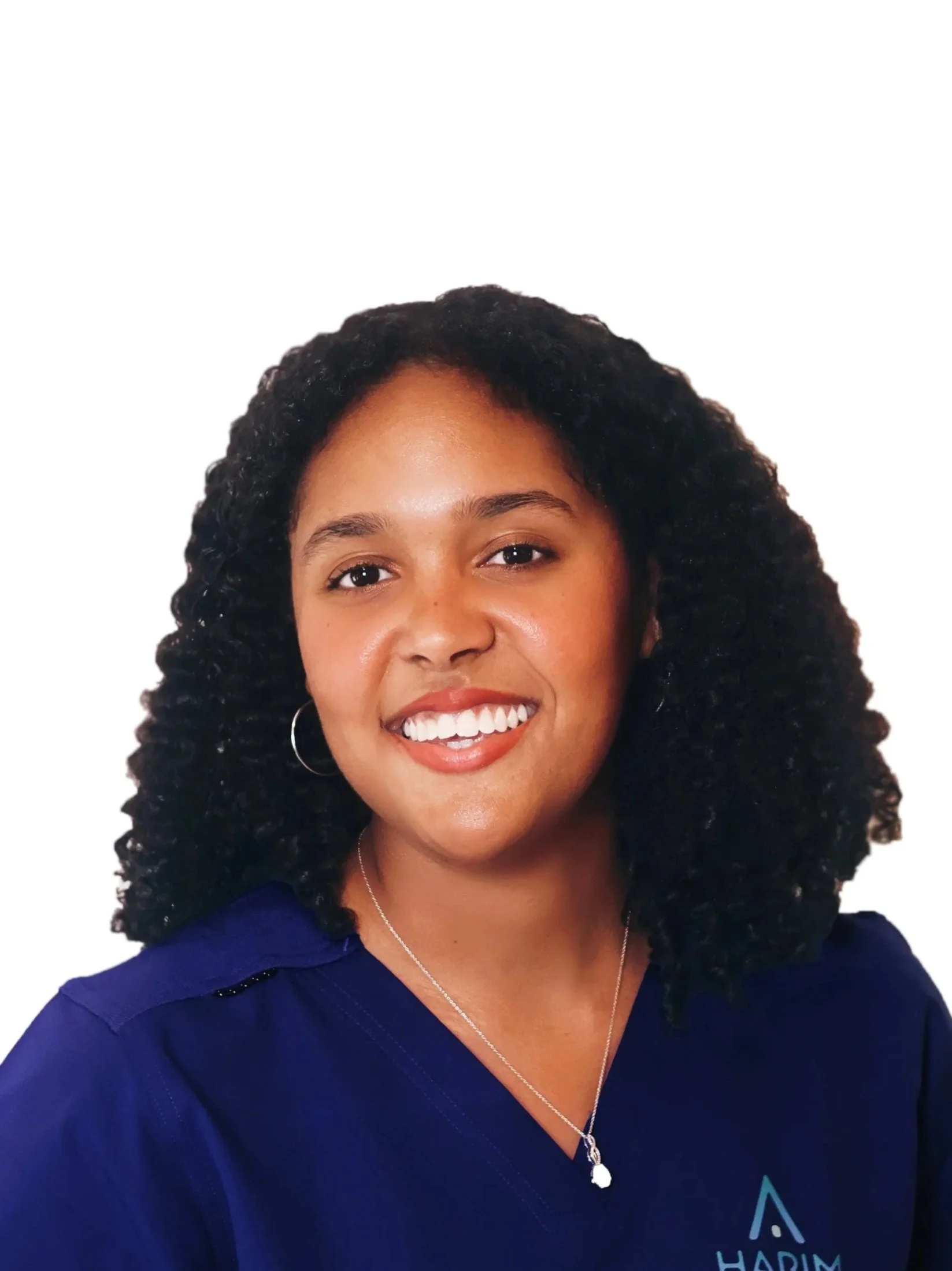 Portrait of a woman with dark curly hair, smiling, wearing a navy blue shirt with a logo and a silver necklace with a pendant.