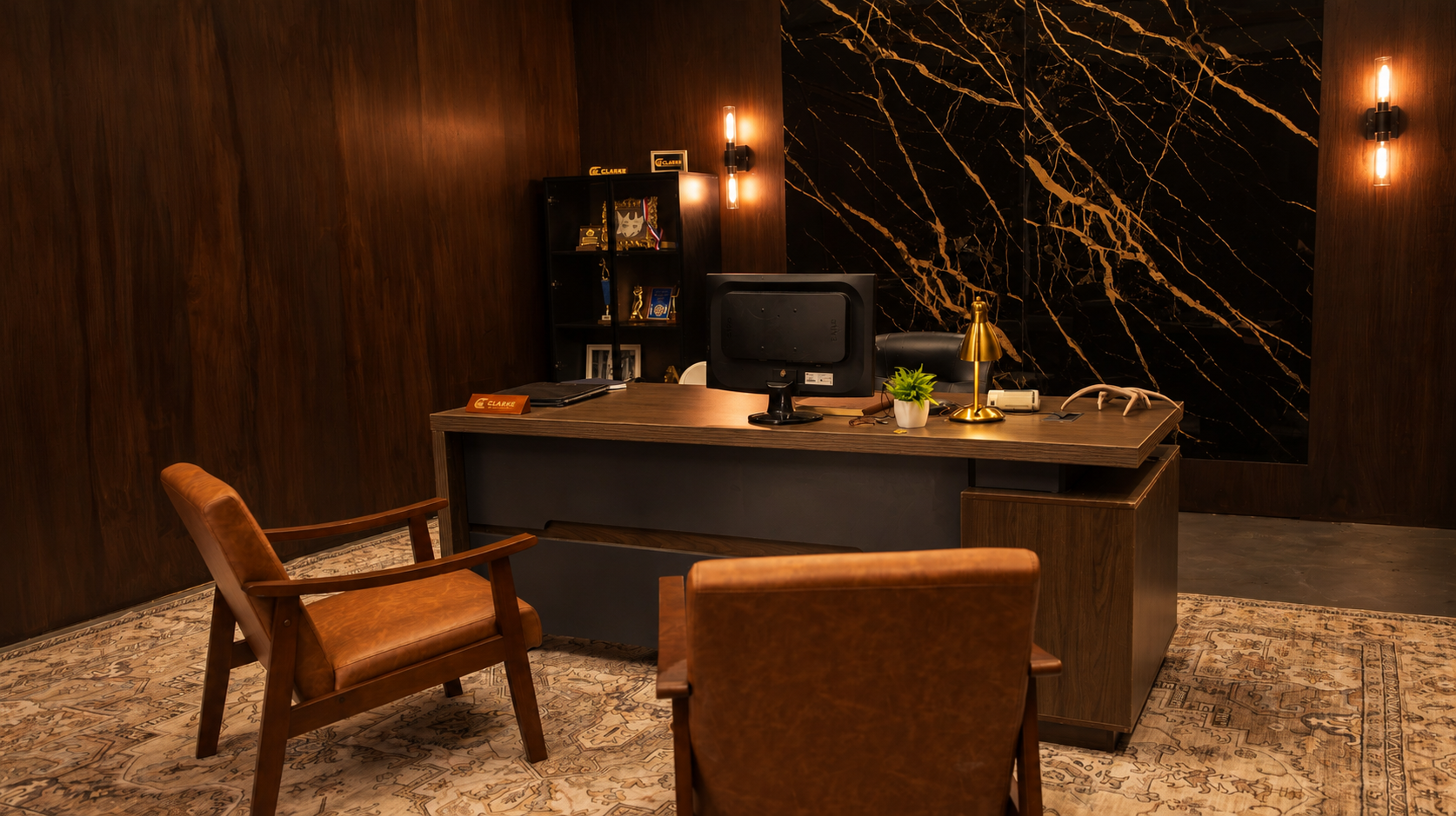 Office with dark wood walls, a large wooden desk with a computer monitor, gold desk lamp, potted plant, and accessories. Two leather chairs face the desk. A black shelf with awards and framed photos stands behind the desk. The wall behind the desk features black marble with gold veining, and the floor has a patterned rug.