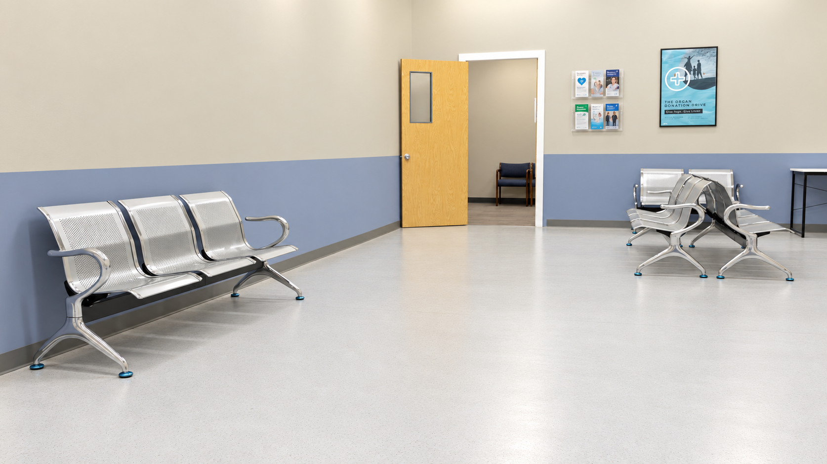 Empty waiting room in a clinic or hospital with metal chairs, a wall-mounted brochure rack, and a framed poster on the wall.