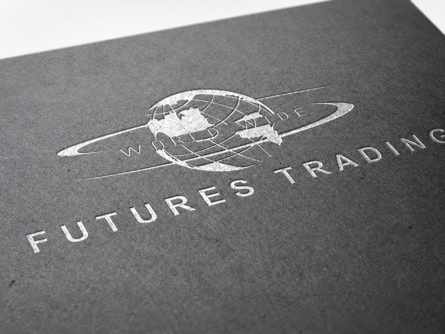 Close-up of a gray paper with an embossed logo of a globe with rings, planets, and lines, and the text 'World Trade Futures Trading' beneath it.