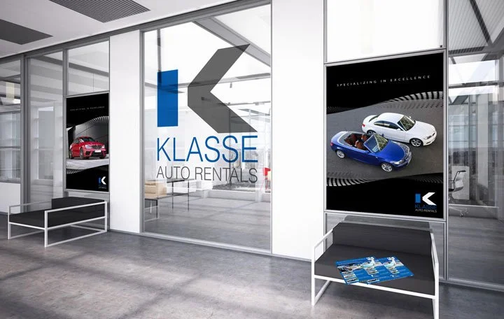 Interior of a car rental office with advertisements of luxury cars, a glass wall, and a bench with a brochure.