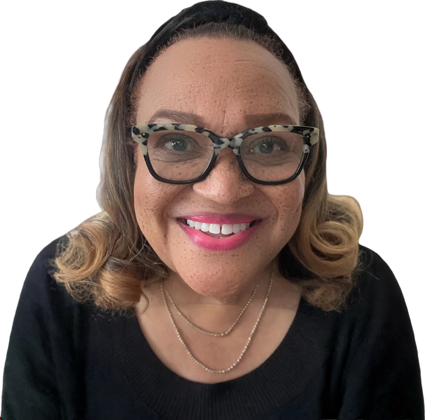 Smiling woman with light skin, curly blonde hair, wearing tortoiseshell glasses, a black top, and necklaces, against a black background.