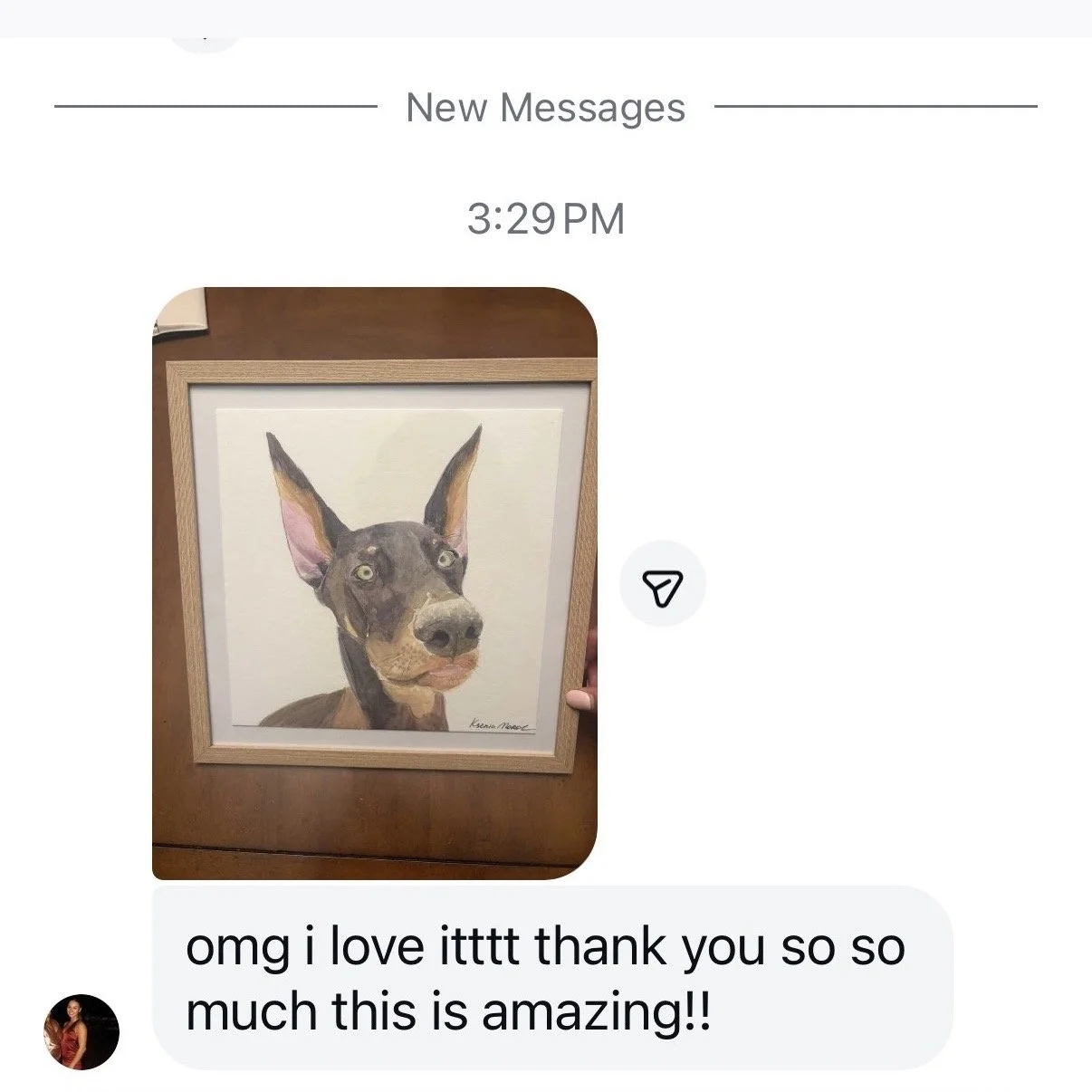 A framed watercolor painting of a dog with large ears and expressive eyes on a wooden surface, with a person’s hand holding the frame.