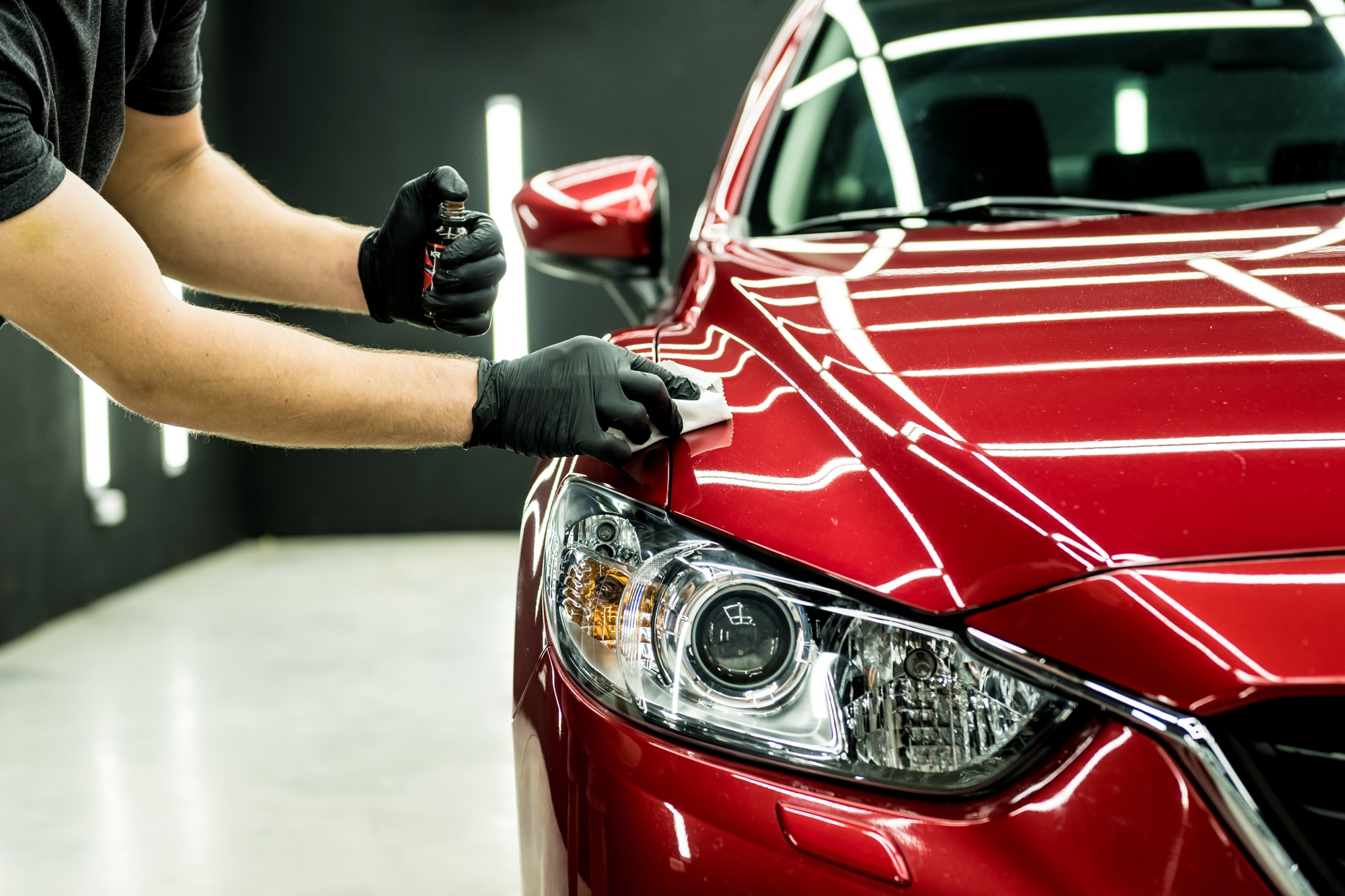 A person wearing black gloves cleaning or detailing a shiny red car in a professional garage or detailing shop.