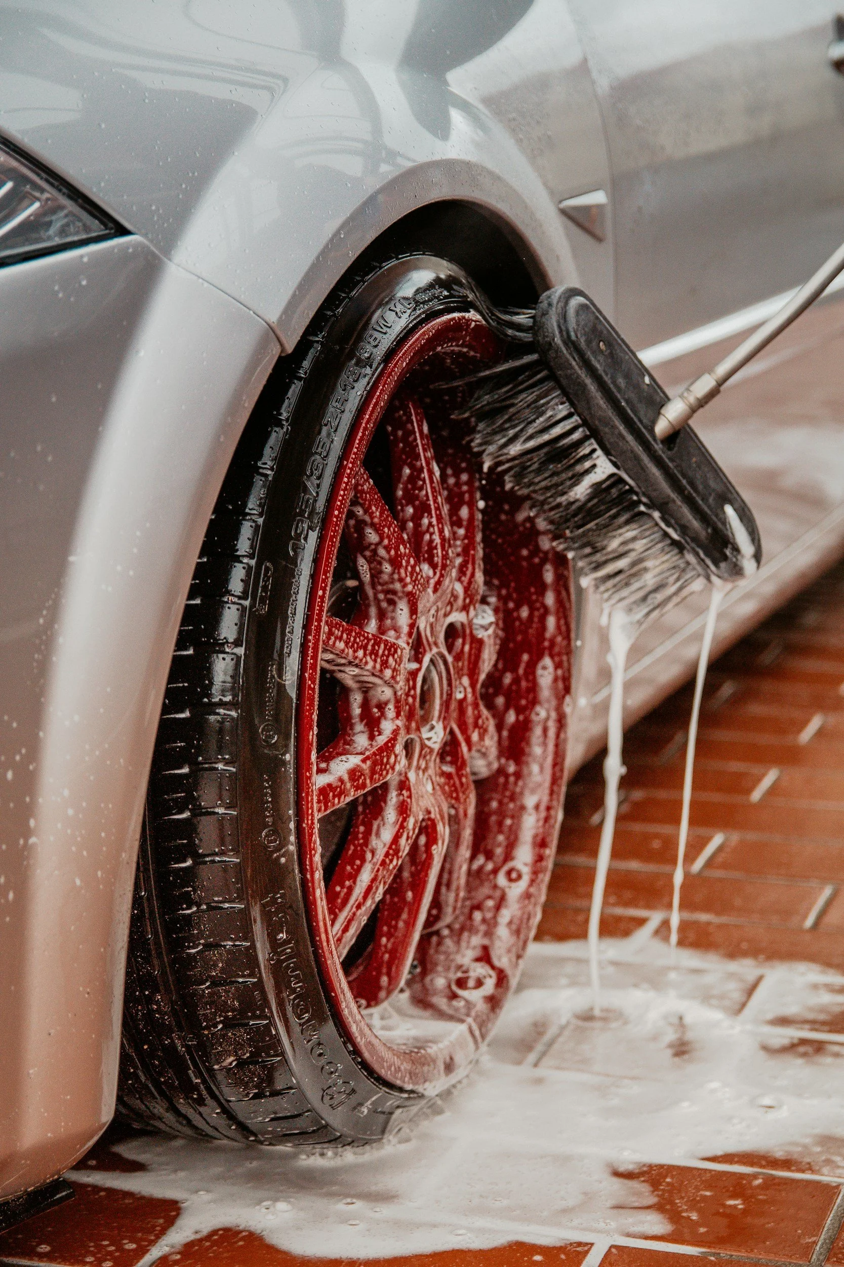 Washing a car's tire and rim with soap and a brush on a tiled floor.