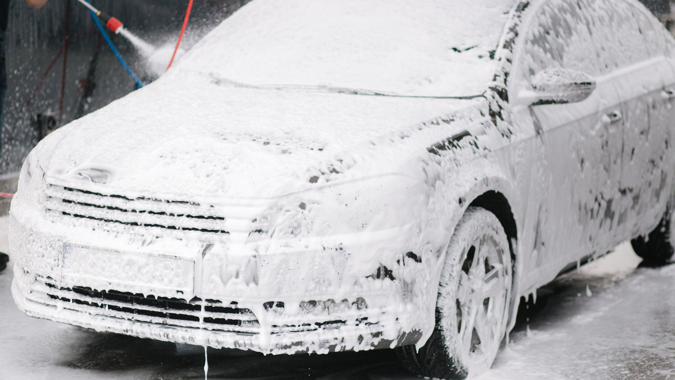 Car covered in soap and foam during car wash in snowy weather.