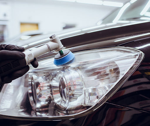 Person cleaning or polishing a car's headlight with a handheld polishing tool in a garage