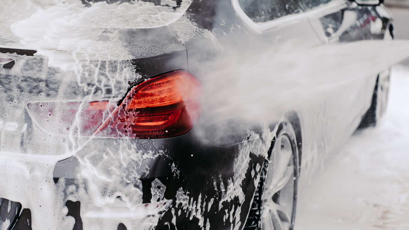 A black car being washed with soap and water, snow or ice on the ground.